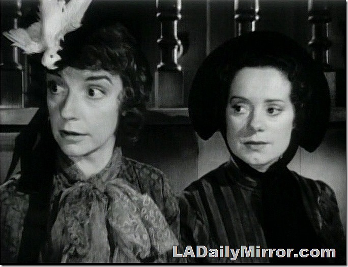 Two women in Victorian costumes. One is wearing a hat with a bird perilously perched on it. The other wears a bonnet. Two women in Victorian costumes. One is wearing a hat with a bird perilously perched on it. The other wears a bonnet.