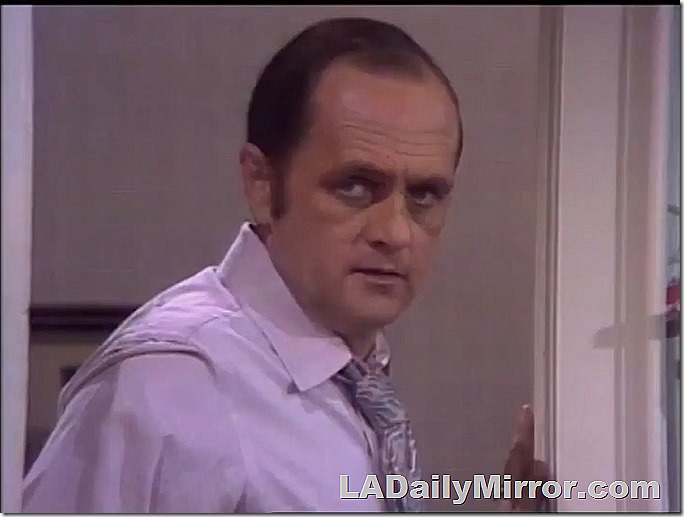 Man in lavender shirt, tie pulled loose, standing from doorway. 