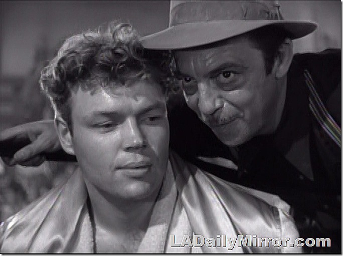 Two men, conferring. One man is whispering in the other man's ear. 