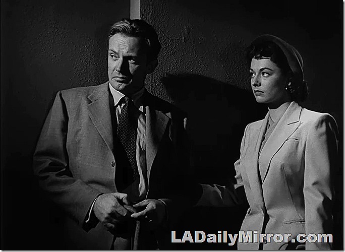 Man in coat and tie with woman in elegant suit and hat. 