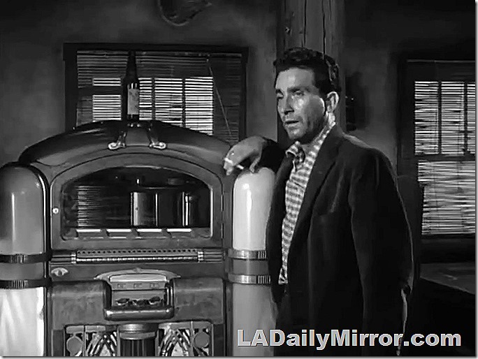 Man smoking a cigarette and leaning on a juke box.