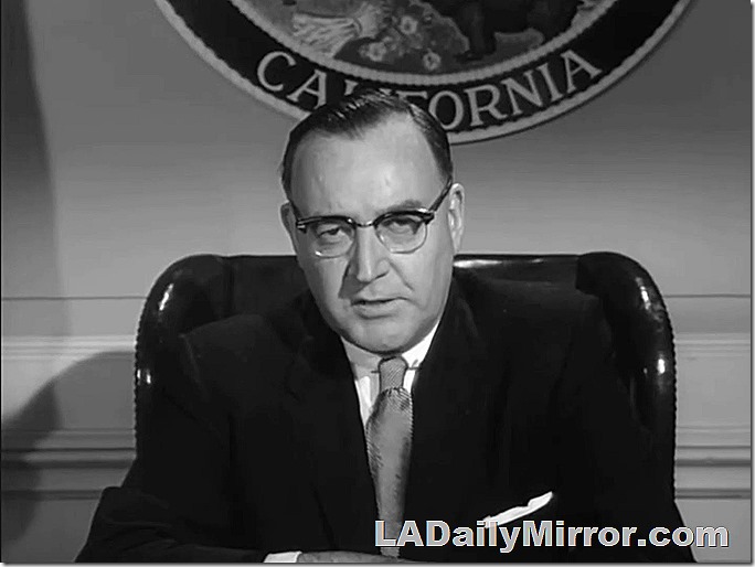 Man wearing a suit, sitting at desk. 