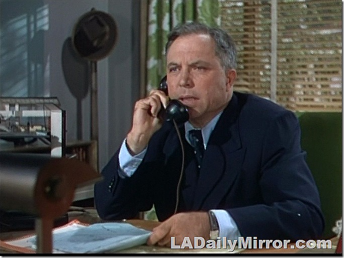 Man in suit at desk, talking on telephone. 