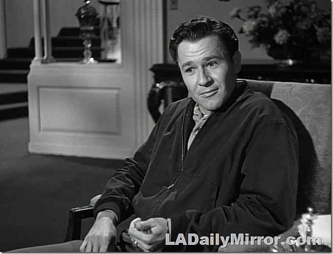 Man in windbreaker, sitting in chair. 