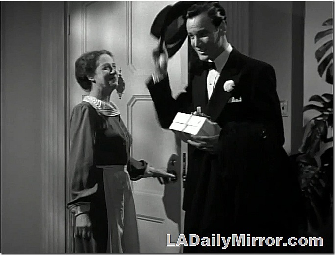 Man in tux, takes off his hat as a woman dressed as a maid smiles. 