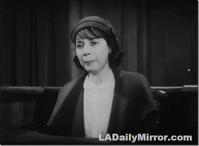 Woman in hat and suit. She has a pensive expression. 