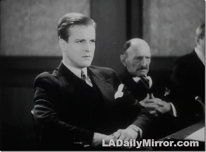 Man in suit with wide lapels. A kerchief in his pocket. He is looking intently. 