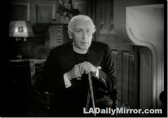 Man with white hair, wearing clerical collar. He's sitting and holding a cane 