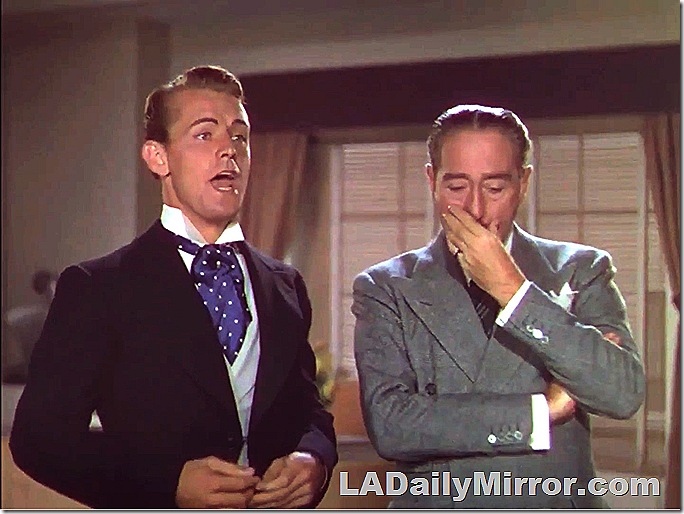 Man in wing collar. Singing. Man in double-breasted suit, listening. 