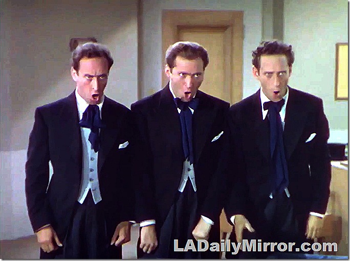 Three men, singing. They are wearing dark blue coats, vests and loose neckties. 