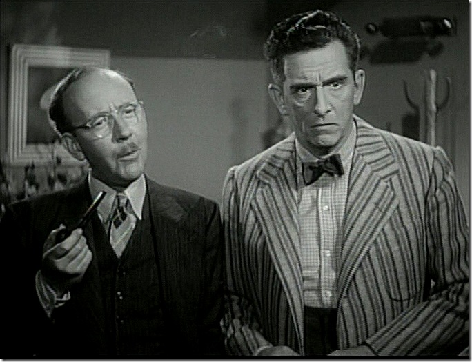 Man wearing glasses and smoking a pip. His companion has a loud sport coat and a tiny bow tie. 