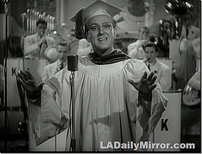 Man in cap and gown, wearing glasses. 