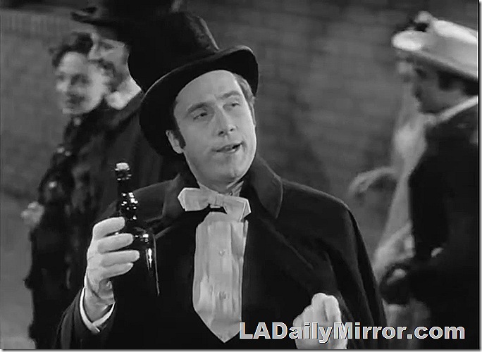 Man in top hat and cape holding a bottle. 