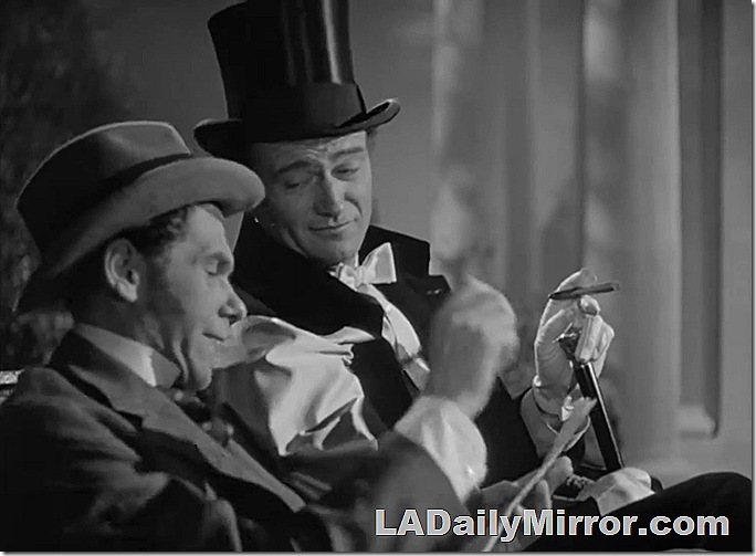 Man in top hat and cape, smoking a cigar. His companion wears a coat and hat with long sideburns. 