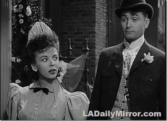 Woman in servant's outfit and man in derby with high color and flower in lapel. 