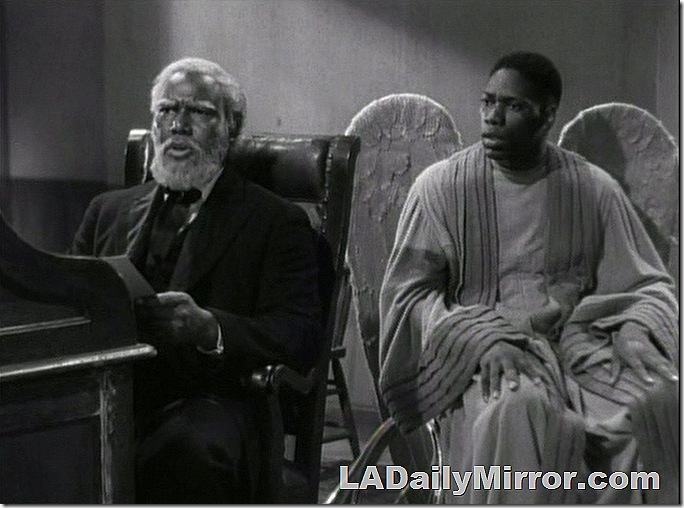 Bearded man sitting at desk. An angel is next to him. 