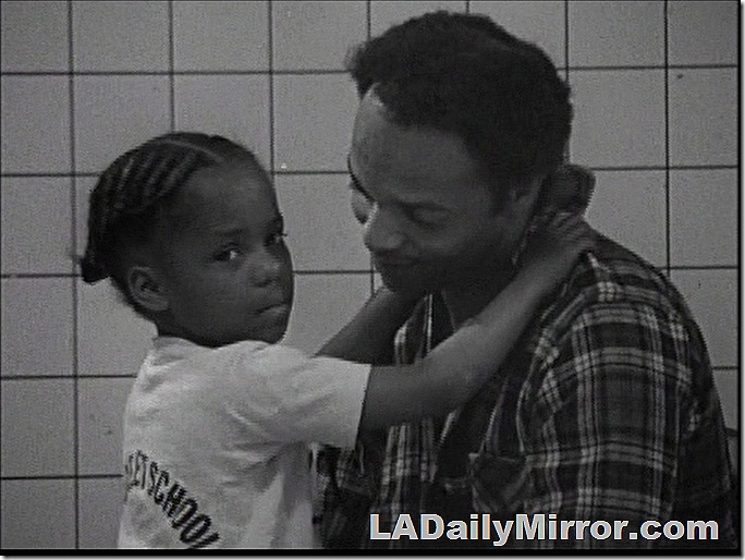 Young girl with her hands around her father's neck. He's looking at her while she's looking at the camera. 