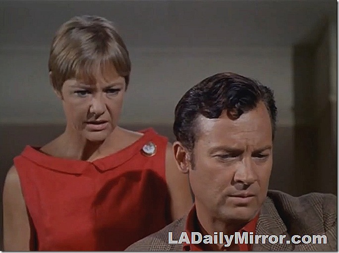 Woman with short hair in sleeveless dress. Man in sport coat and shirt. They are looking at something in alarm. 