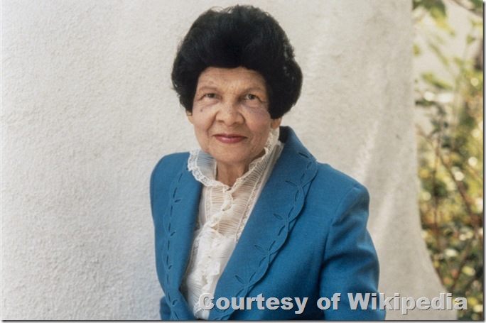Woman in teal suit and frilly necked blouse.
