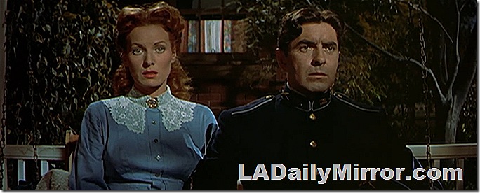 Man in Army uniform sitting with woman in blue dress, lace collar and long red hair. 