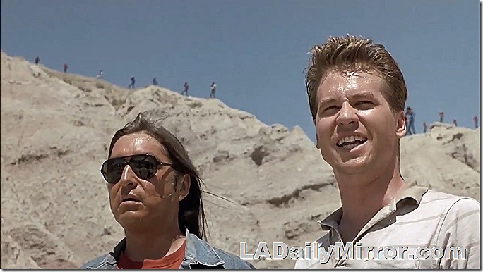Two men in canyon. The first man has long hair and wears sunglasses. The second has short hair and wears a polo shirt. 