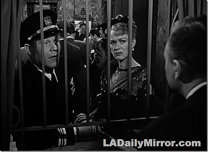 Officer and elegantly dressed lady at a ticket counter. 