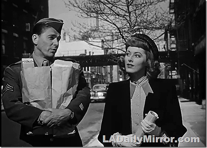 Soldier carrying bags of groceries, talking to a lady companion. 