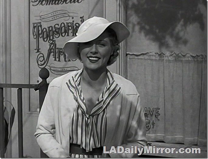 Woman in broad-brimmed hat and open-necked blouse. She's smiling. 