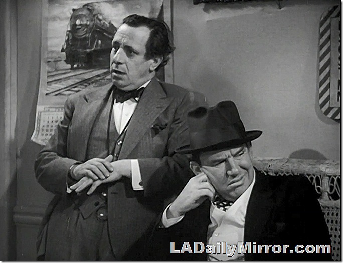 Two mysterious fellows. One is wearing a three-piece suit, the other is wearing a porkpie hat. 