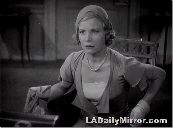 Woman in chair, wearing a dress, gloves, hat and necklace. 