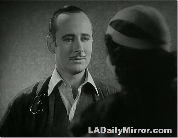 Man with slick hair and pencil mustache is dressing gown. With Back of the Head Woman. 