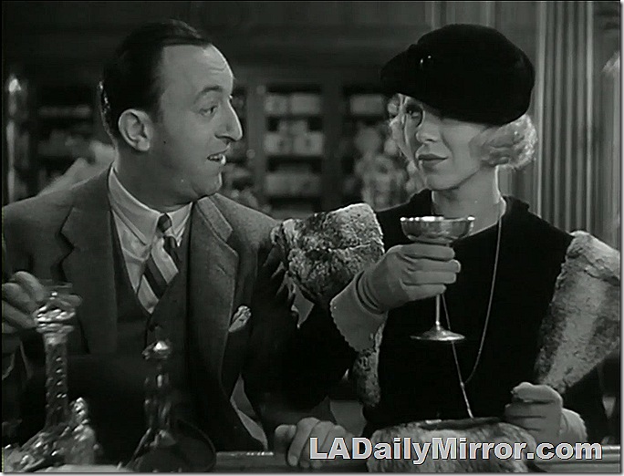 Man and woman at a bar. She is elegantly dressed, wearing gloves and holding a silver goblet. 