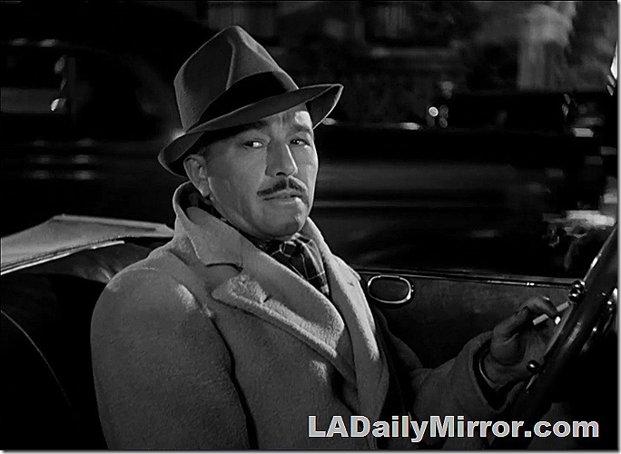 Man in coat and hat at wheel of convertible. 