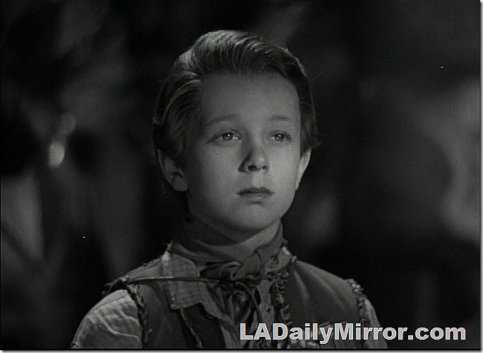 Boy with longish hair, wearing a vest and bandana. 