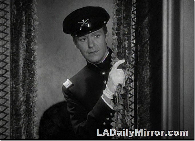 Man in military uniform peering around drapes.