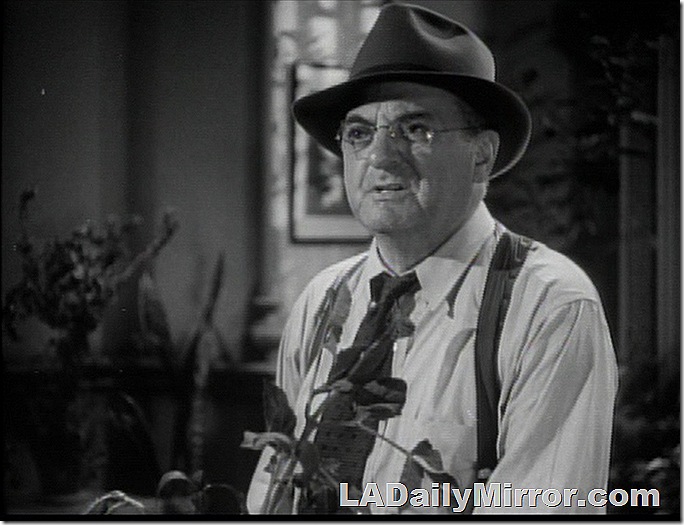 Man in shirt sleeves, suspenders, tie and hat, with glasses. 