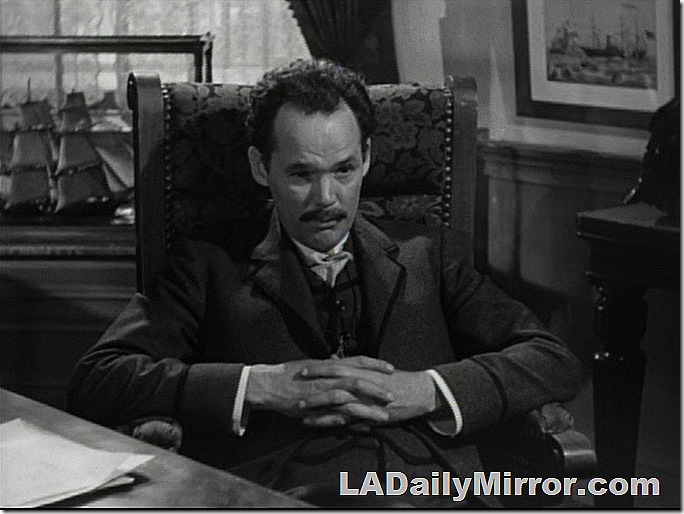 Man with mustache sitting at desk, his hands interlaced 