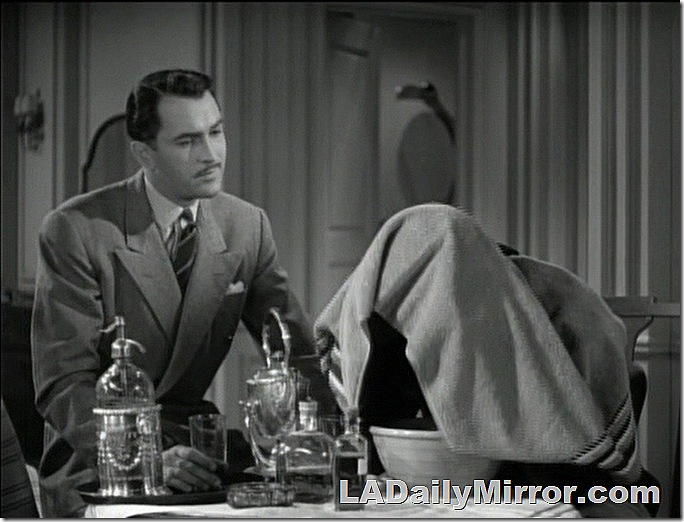 Man in double-breasted suit watches man with head under towel Man in double-breasted suit watches man with head under towel