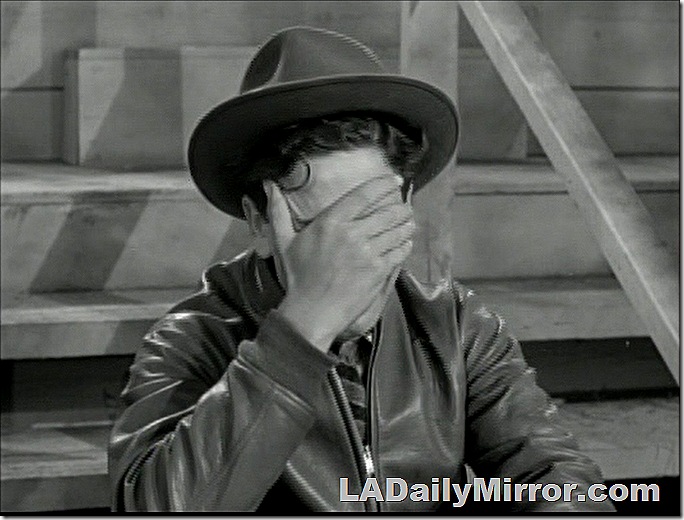 Teenage boy in hat and jacket, covering his eyes with one hand. 