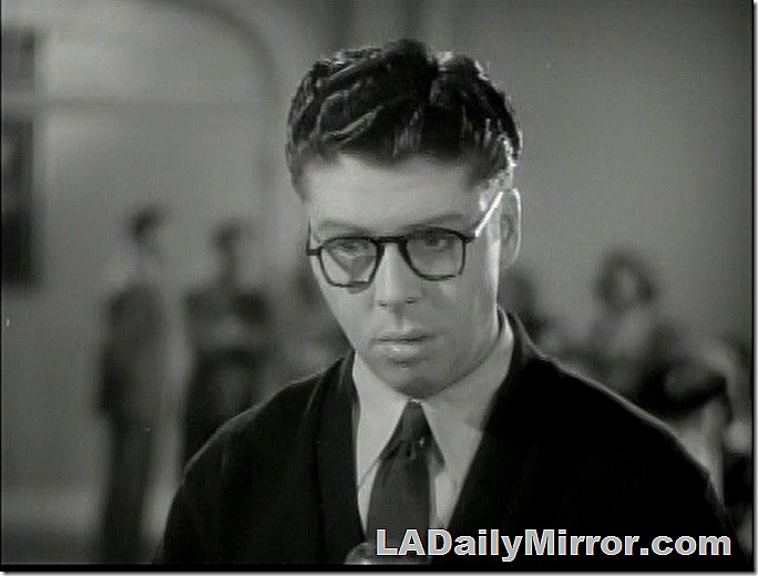 Young man wearing glasses, in sweater and tie. 