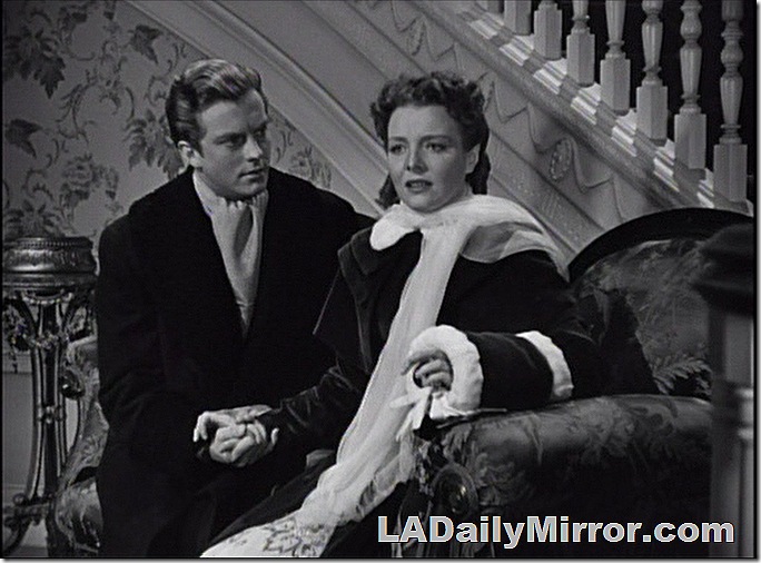 Man and woman dressed for winter weather, sitting on period couch. Man and woman dressed for winter weather, sitting on period couch.