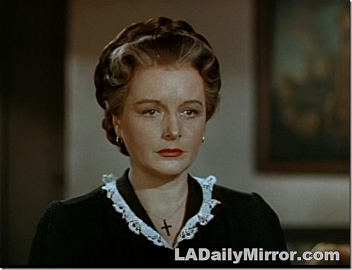 Woman with her hair up, a small lace decoration at the collar. She's wearing a necklace with a cross. 