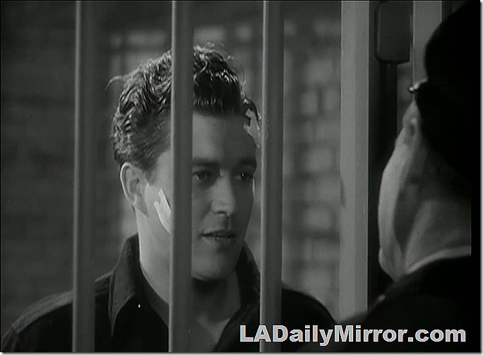 Man in a jail cell with a bandage on his cheek. 