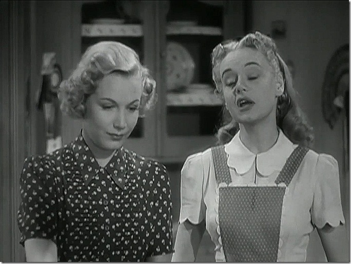 Two women. One wears a dress with a patterned fabric, the other wears an apron. 