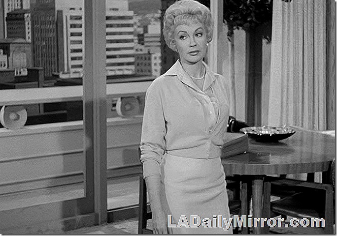 Woman wearing skirt and sweater, with short hair and earrings. 