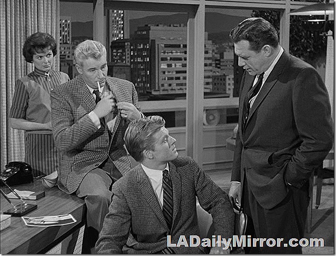 Mysterious grouping. A man sitting in a chair talking to a man in a suit, as a man and a woman observe. 