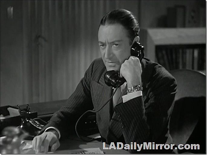 Man in double-breasted suit, hair parted in the middle, talking on the phone. 