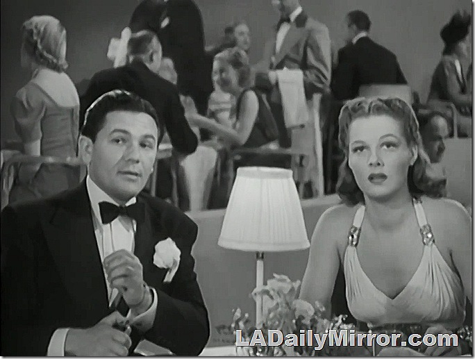 Elegantly dressed man and woman at table in nightclub. 
