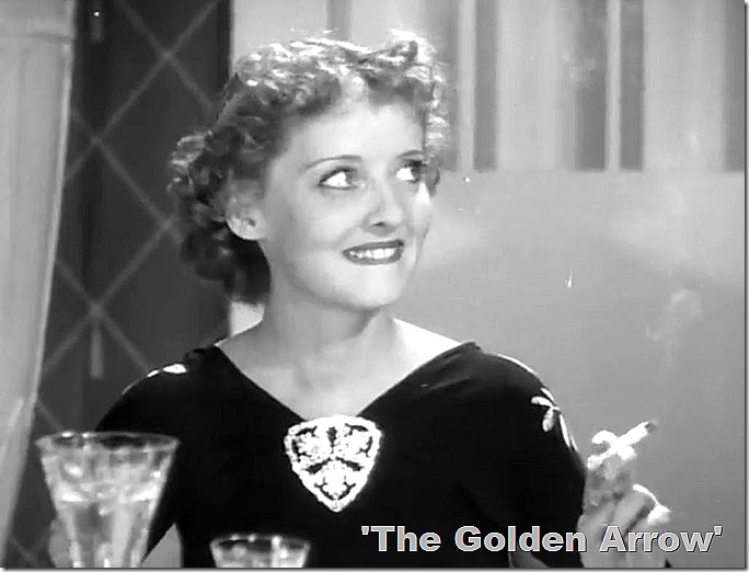 Bette Davis with glittery 'fascinator at the neckline of her dress. She's smoking a cigarette. 