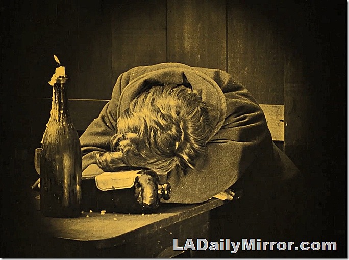 Man asleep at a table, his head on his arms. A candle stuck in a bottle burns low. Man asleep at a table, his head on his arms. A candle stuck in a bottle burns low.